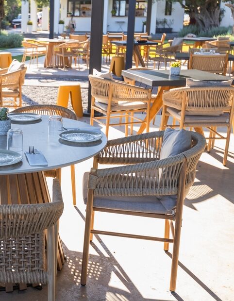 Commercial outdoor restaurant patio with dining tables, woven chairs, and hospitality furniture arranged for guests.