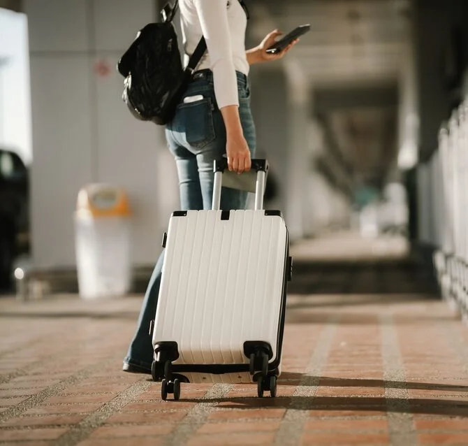 International student traveling with luggage and a smartphone for study abroad.